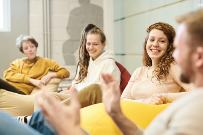 Four people sit in beanbag chairs. Three people are watching the fourth speak. They are all smiling.