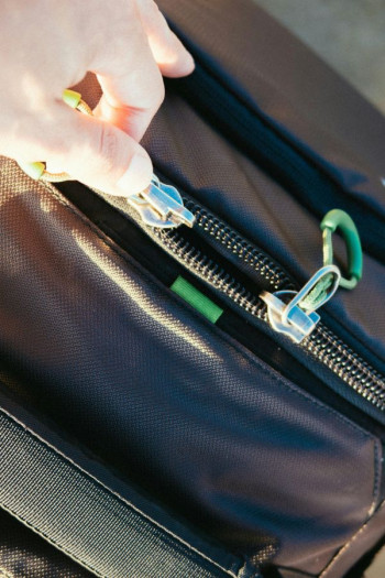 A hand unzips a black leather bag.