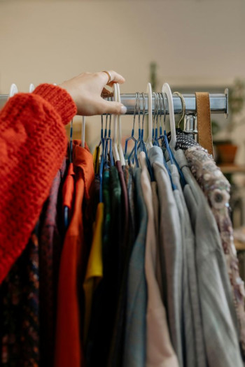 A hand hovers over a rack of clothes on a rack. They are all mixed so look like charity clothes.