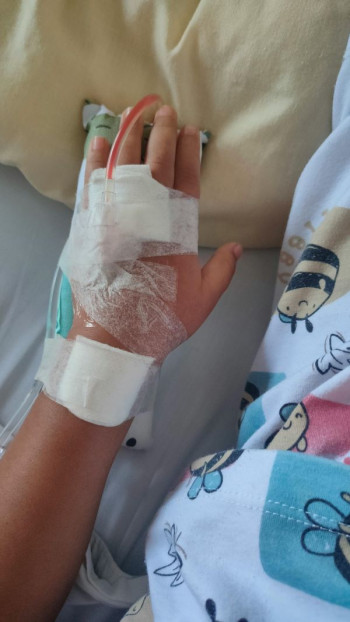 A child's hand is wrapped in medical bandages and tubes. It looks like the child is in hospital although we can only see a close up of the hand and some pyjamas.