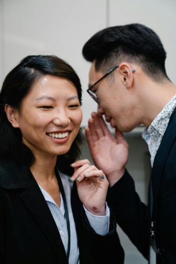 An Asian man with a floral shirt gossips with an Asian woman wearing corporate clothes.