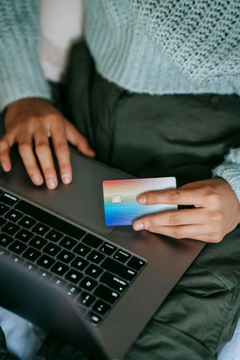 A woman's hands are on an open laptop and she holds a credit card.