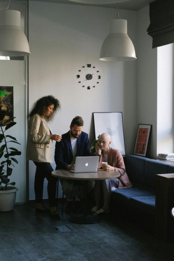 Three people sit around a laptop having a meeting.