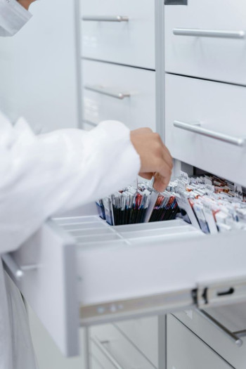 A person in a white coat goes through a file drawer of records
