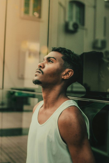 A frustrated looking man in a singlet leans against a building