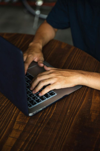 A man's hands are using a laptop on a round wooden table.