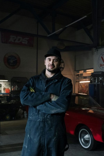 A mechanic stands looking at the camera with his arms folded