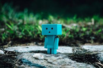 A small blue boxy robot stands outside on rocks