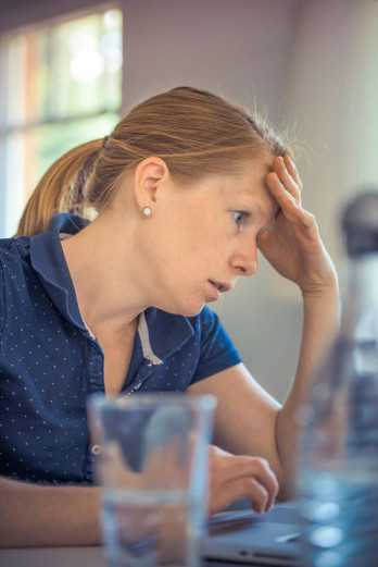 A red headed woman sitting at a desk has her head in her hand looking stressed.