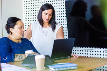 Two Maori women sit looking at a computer