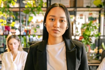 A close up of an Asian woman dressed in a business suit with a white tshirt