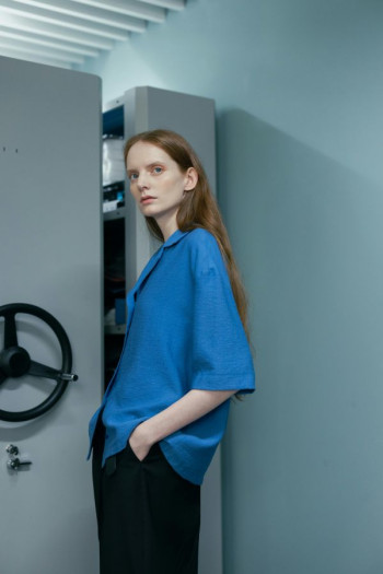 A white woman with long red hair wearing a blue shirt stands next to a lundia filing unit.
