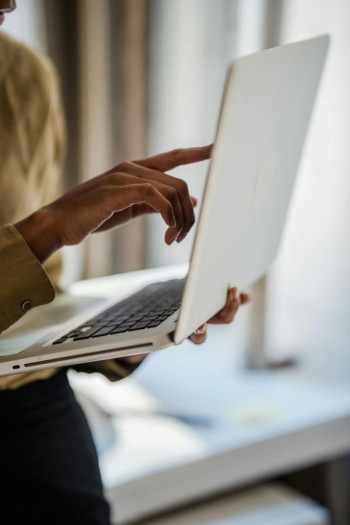 A close up image of a woman's body shows her hand pointing at the laptop she is standing and holding.