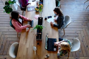 Three women work at laptops at a long shared table