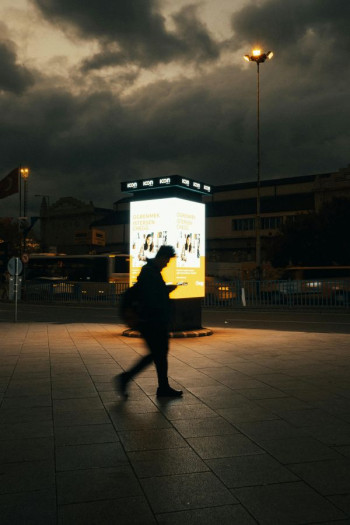 A person walks in shadow in front of a freestanding billboard bollard.