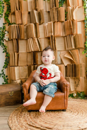 A child sits in a small chat wearing a spiderman t-shirt and denim shorts. He looks happy.