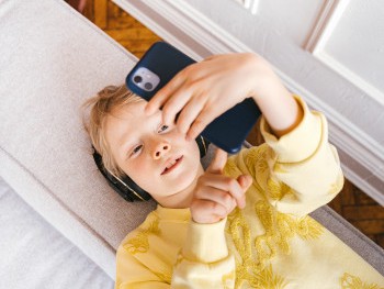 A child of about nine lies on the floor using a smartphone above their face. Their top is yellow.