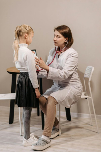 A small blonde haired girl has her heart checked by a doctor