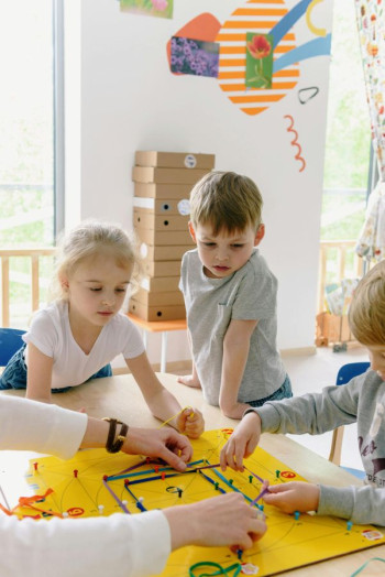 Three white children play inside on a board game
