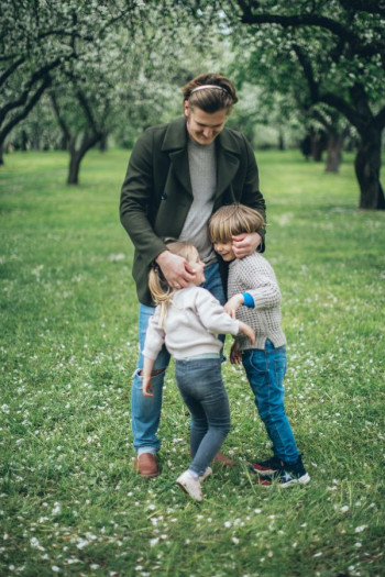 A man stands in an orchard with two small children
