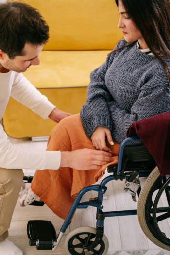 A man kneels down to help a woman sitting in a wheelchair