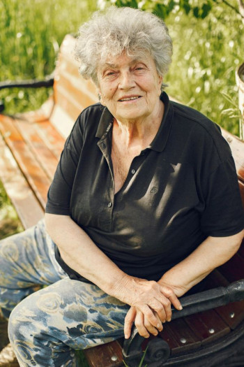 An elderly woman sits on a part bench looking at the camera.