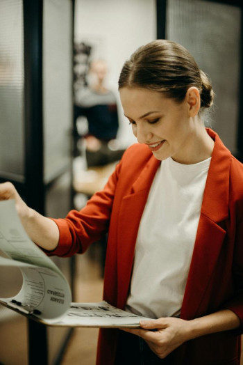 A woman in a red blazer looks as a clipboard of information and is smiling