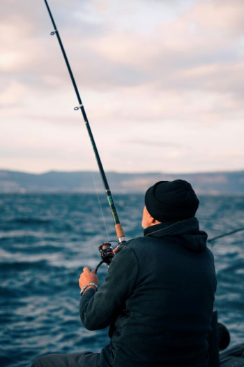 A man in black clothing faces away from the camera fishing with a fishing rod.