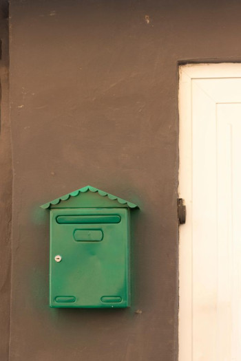 A green mailbox mounted on a brown wall near a white door