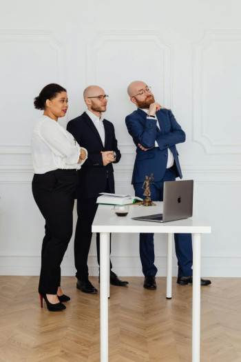A group of three lawyers stand looking into the distance beside a white table