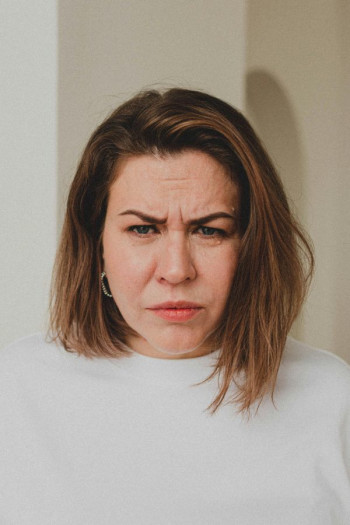 A grumpy woman with a long brown bob haircut looks at the camera.