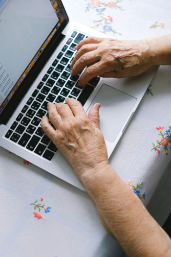 A white persons hands on a laptop keyboard. The laptop is on top of an embroidered cloth.