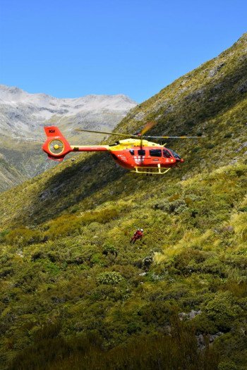A rescue helicopter flies over a bushclad mountain
