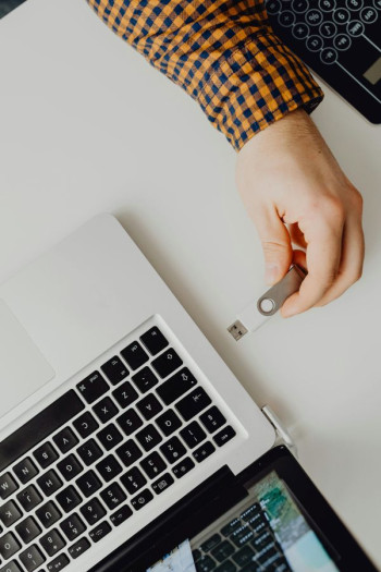 A hand wearing a checked shirt puts a USB stick into a laptop