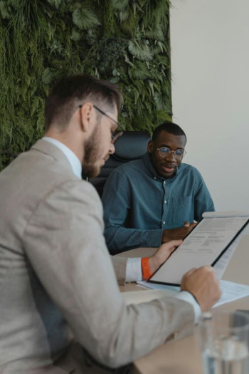 A man sits being interviewed by another man in a corporate setting.