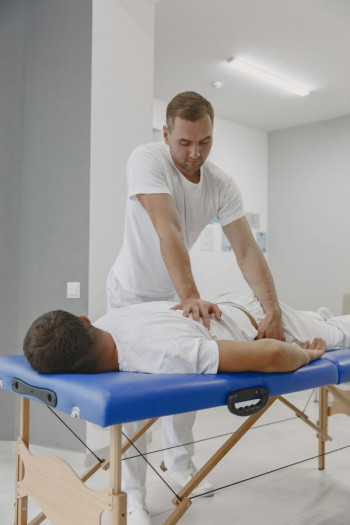 A man in white clothes lies on a blue massage table with another man in white touching him