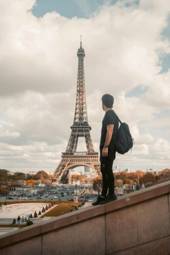 A man stands on a sloping wall looking at the Eiffel Tower in Paris
