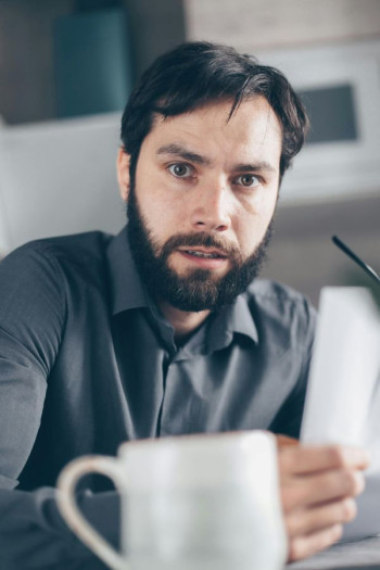 A white man with dark hair and beard holds a letter and looks panicked