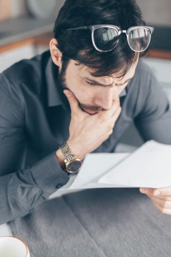 A white man with dark hair leans over two documents looking concerned