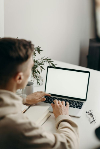 A young man faces away from the camera and is working at a laptop.
