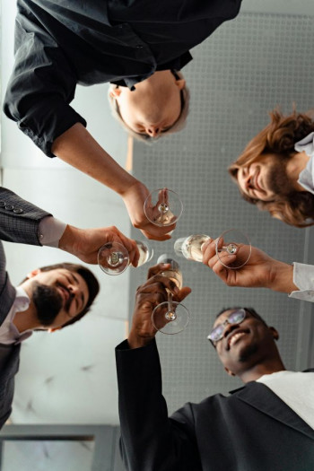 Four men in corporate clothing stand holding wine glasses. The view is from under the wine glasses.