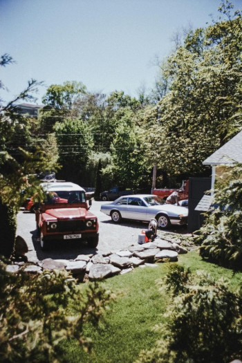 A neighbourhood scene showing a a green cul-de-sac and garden with two cars parked 