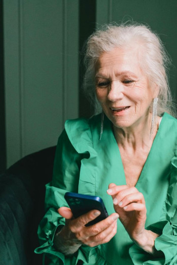 An older woman wearing green uses a smart phone.