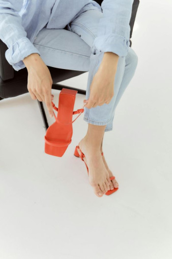 A woman in blue jeans tries on orange strappy sandals