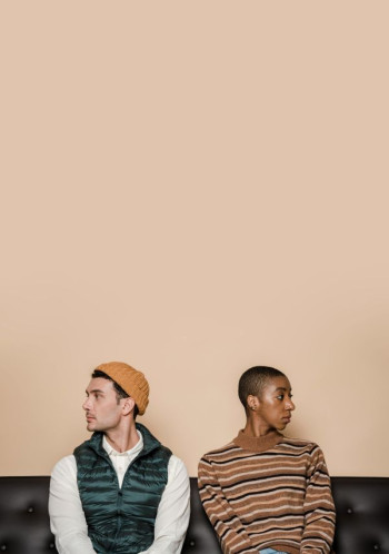 An unhappy couple sit on a couch looking in opposite directions