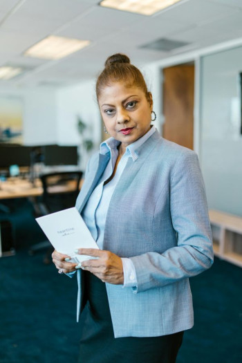 A middle aged woman in a blue blazer stands in an office holding a greeting card