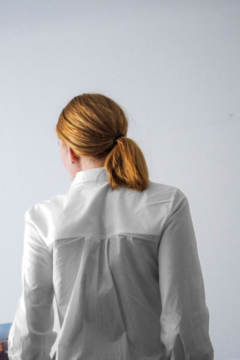 A woman in a white shirt with a red ponytail is turned away from the camera