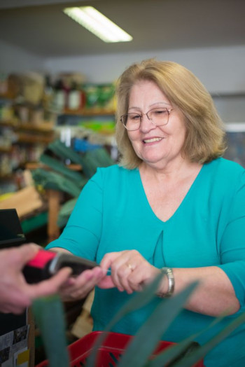 A middle aged woman in a teal top with shoulder length blonde hair uses an eftpos machine in a shop