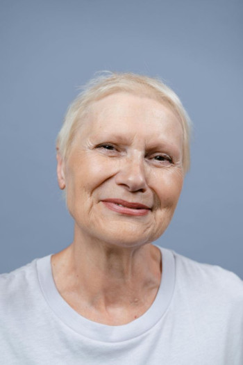 A middle aged woman has blonde short hair and a light coloured top. She is smiling.
