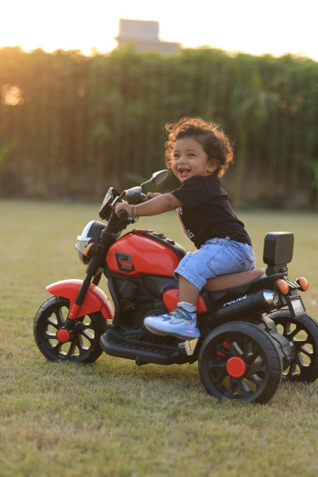 A smiling child sits on a toy tricycle in a field.